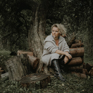 Aktorka siedząca na pniu drzewa.