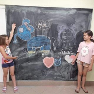 Dwie dziewczynki prezentują namalowany na tablicy rysunek