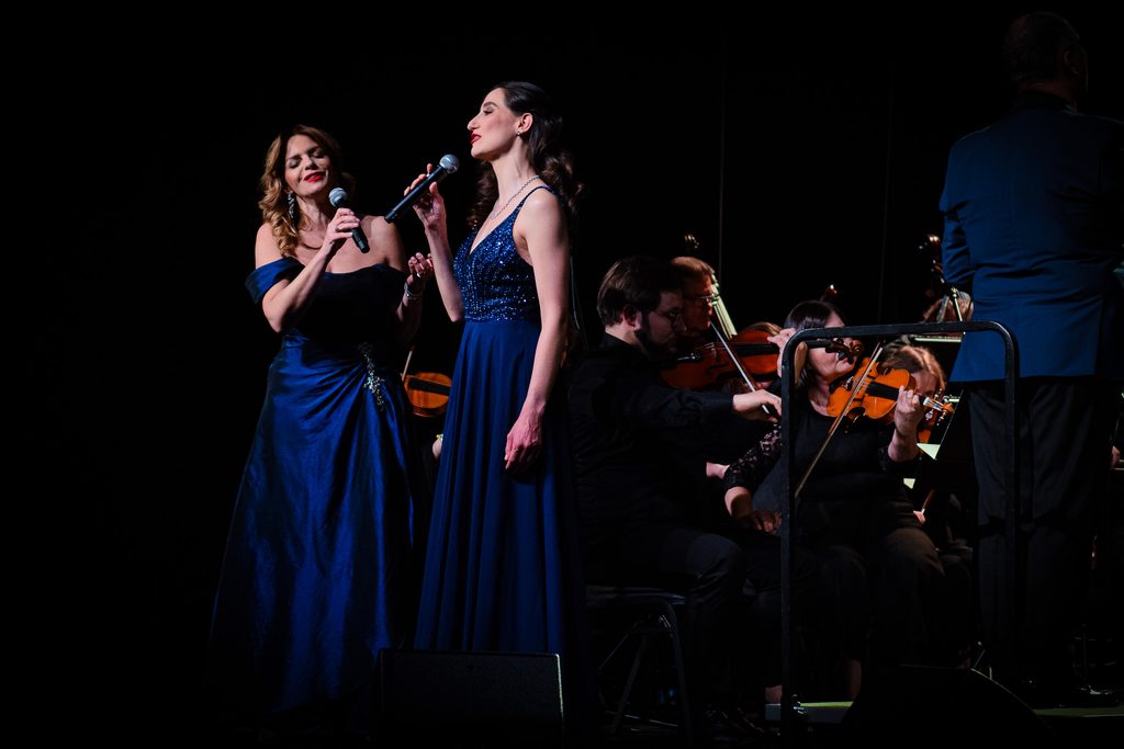 Zdjęcie przedstawiające orkiestrę Filharmonii Krakowskiej wraz dwiema solistkami.